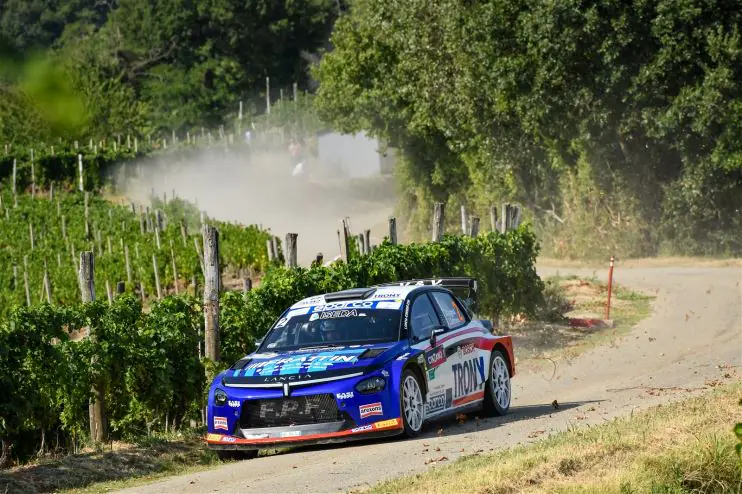 Due rally car in assetto di gara su una strada di montagna ligure con spettatori sullo sfondo, al Rallye Sanremo